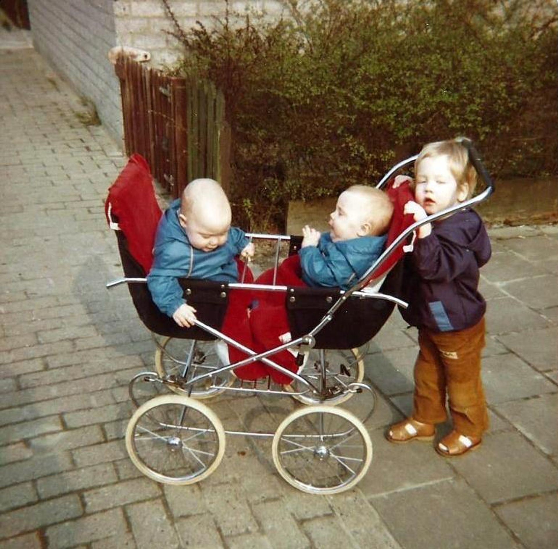 Pim bij de kinderwagen waar zijn zusjes Annemiek en Frederiek in zitten