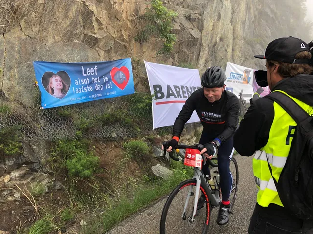 Jurgen fietst Alpe d'Huzes, met aan de zijkant op een berg een spandoek met een foto van zijn dochter en de tekst: Leef alsof het je laatste dag is.
