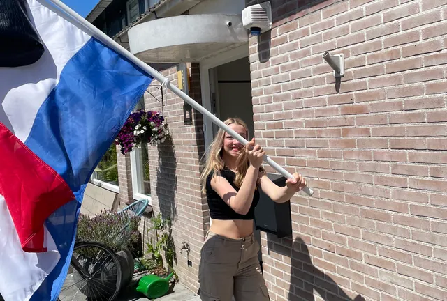 Esthers dochter Isa staat met de Nederlandse vlag in haar handen, waar haar schooltas aan hangt.